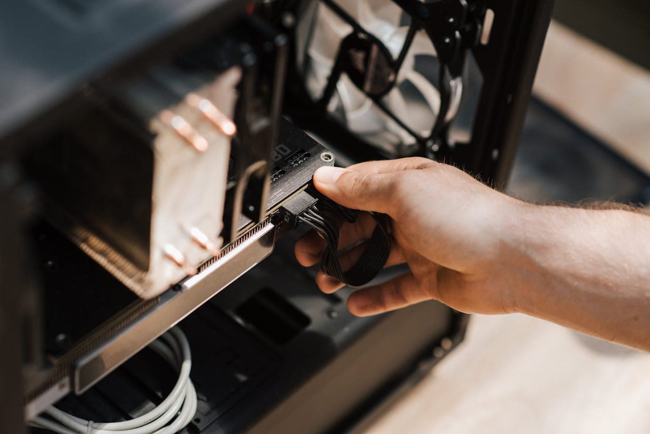 Hand inserting a GPU into a PCIe x16 slot inside a PC case with power cables attached
