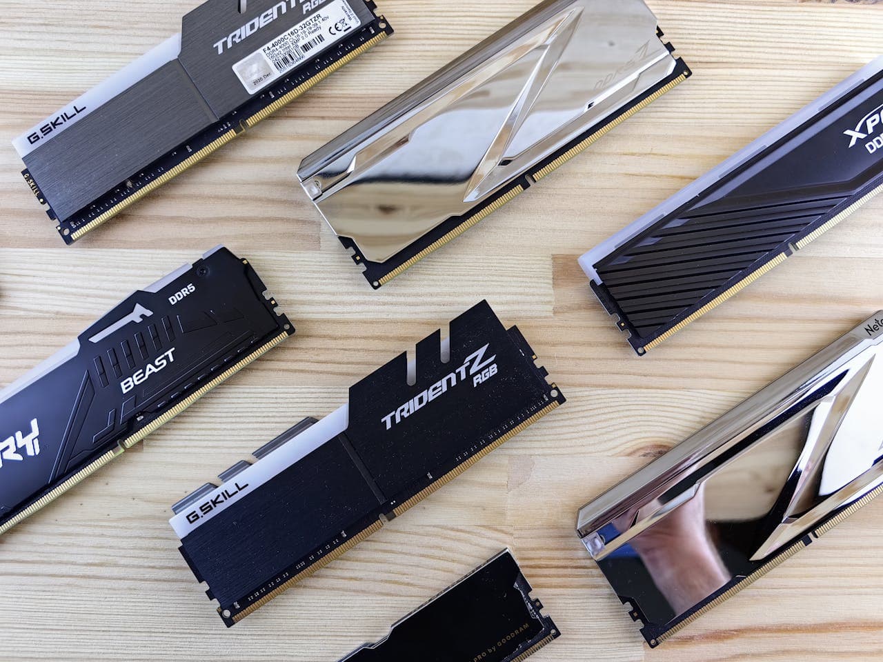 Multiple DDR4 and DDR5 RAM sticks from various brands laid out on a wooden surface, including G.Skill Trident Z RGB and Kingston Beast DDR5