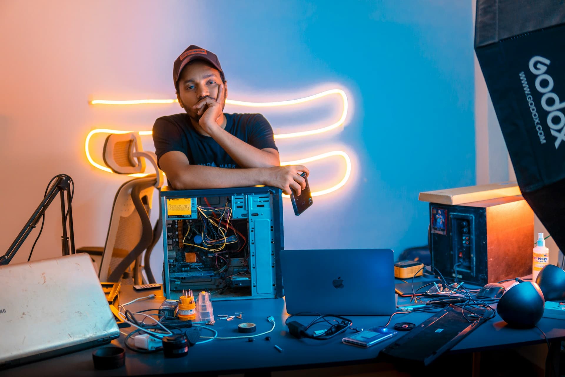 Man sitting at a cluttered desk, leaning on an open old desktop PC tower with a thoughtful expression, deciding whether to upgrade or replace it